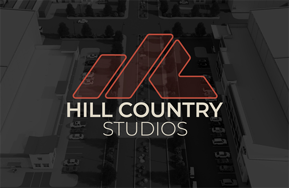 Hill Country Studios logo in orange and white over a dark, desaturated aerial view of a city street.