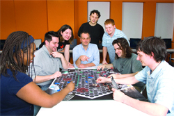 A diverse group of young adults gathered around a table playing a large board game.