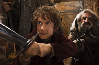 A man with curly hair holds a sword in a defensive pose while others stand behind him.