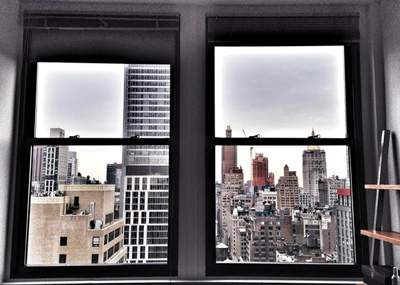 Two large windows overlooking a dense cityscape with various skyscrapers under a cloudy sky.