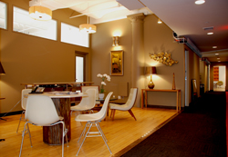 A modern lounge with a round wooden table, white chairs, and warm lighting on a wooden floor.