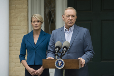 A man in a blue suit speaks at a podium with a woman in a blue blazer standing behind him.