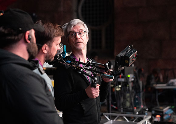Three men on a film set, one holding a large professional camera rig.