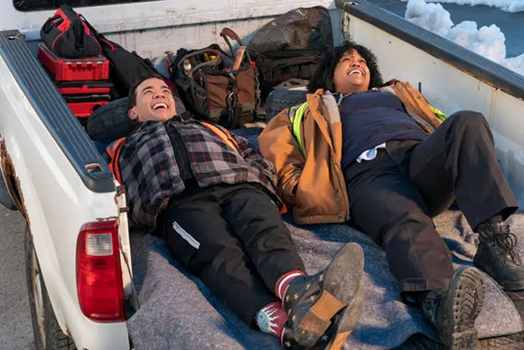 Two people lie in the back of a white pickup truck, laughing together.