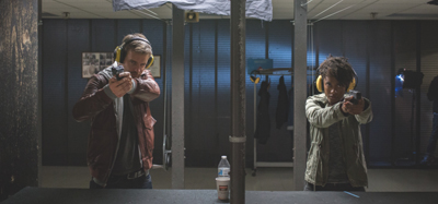 A man and a woman wearing yellow ear protection aim handguns at a shooting range.