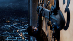 A person reaches up toward the gears of a large clock overlooking a city at night.