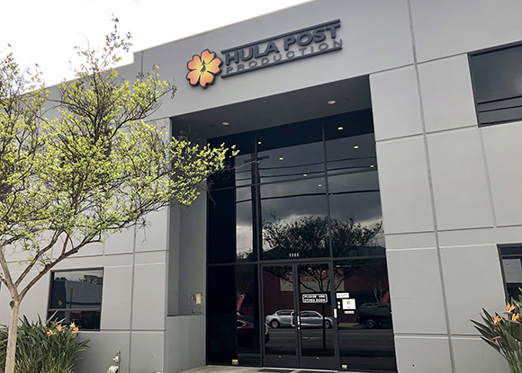The gray facade of Hula Post Production with a flower logo and large glass entrance doors.