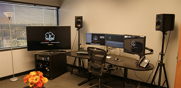 A desk with two computer monitors, large studio speakers, a black office chair, and a large screen in the background.