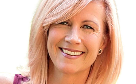 A smiling woman with strawberry blonde hair and blue eyes looking at the camera.