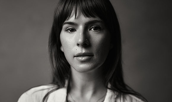 Black and white close-up portrait of a woman with straight hair and bangs looking directly at the camera.