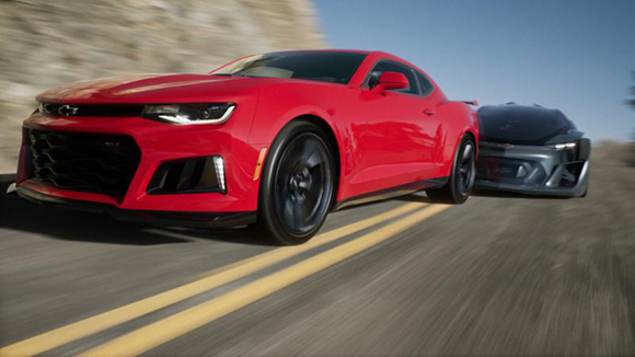 A red Chevrolet Camaro driving fast on a paved road with yellow lines.