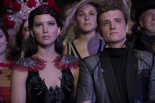 A woman in a feathered black dress and a man in a dark jacket stand among a crowd in costume.