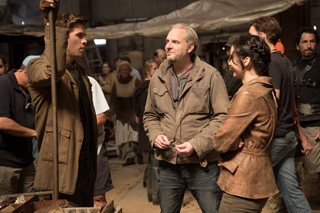 A man in a brown jacket talks to a woman in a leather jacket and a man in a costume holding a staff.