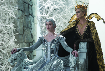Two women in elaborate silver and gold fantasy costumes sit on carved stone thrones.