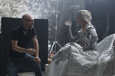 A man in a black shirt talks to a woman in a silver costume sitting on a prop throne.