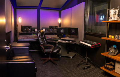 A music studio with a large mixing console, studio monitors, a black leather chair, and a keyboard.