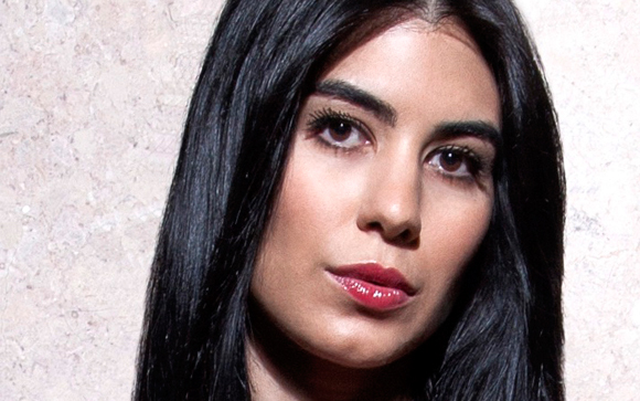 A woman with long black hair and red lipstick looks directly at the camera.