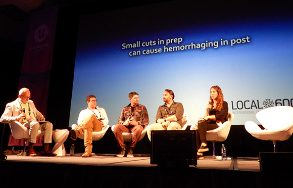 Five people sit in white chairs on a stage in front of a large blue screen with text.