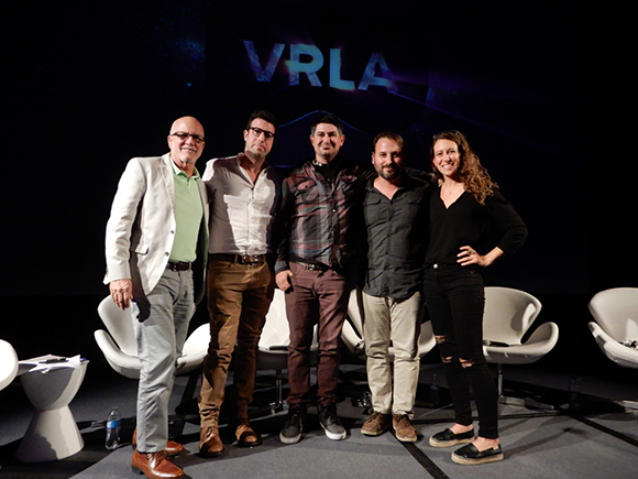 Five people standing in a row on a stage in front of a dark screen with VRLA text.