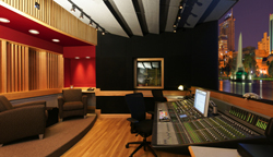 A recording studio control room featuring a large mixing console and a window overlooking a city skyline at night.