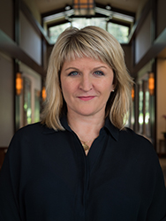 A blonde woman with blue eyes wearing a black button-down shirt, looking forward.