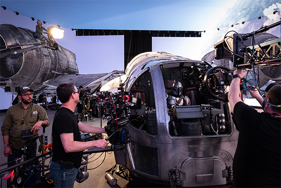 Film crew operating cameras and lighting around a large, detailed spacecraft cockpit set.