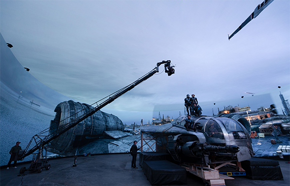 Film crew using a large crane camera to film in front of a massive curved sci-fi landscape backdrop.
