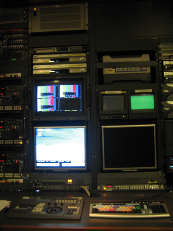 Broadcast control room with multiple monitors displaying test patterns and video feeds, along with various electronic equipme