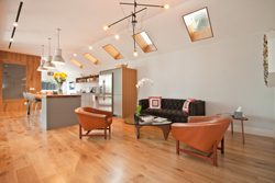 A modern living room with light wood floors, two leather armchairs, a dark sofa, and skylights in the ceiling.