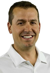 A smiling man with short dark hair wearing a white collared shirt against a white background.
