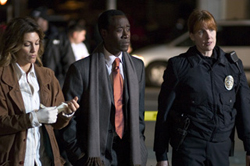 A woman in a brown coat, a man in a suit with an orange tie, and a female police officer walking at night.