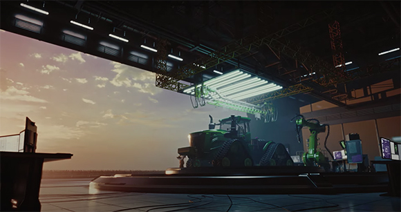 A green tractor on a circular platform inside a large, dimly lit industrial hangar during sunset.