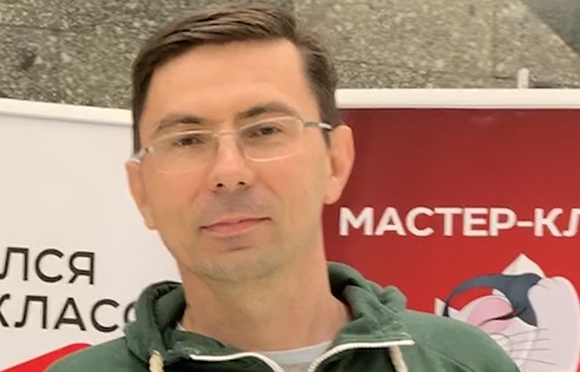 A man with short dark hair and glasses wearing a green zip-up hoodie.