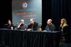 Five people sit behind a black cloth-covered table with microphones during a presentation.