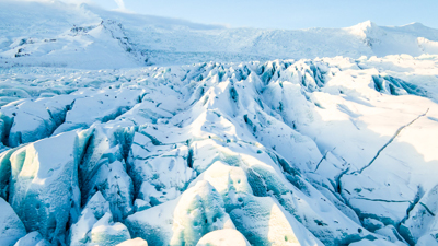A wide view of a massive, blue-tinted glacier with deep crevasses and snow-covered peaks.