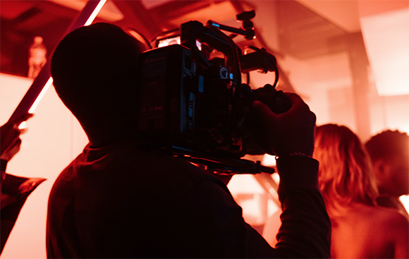 Silhouette of a person filming with a professional camera under intense red light.