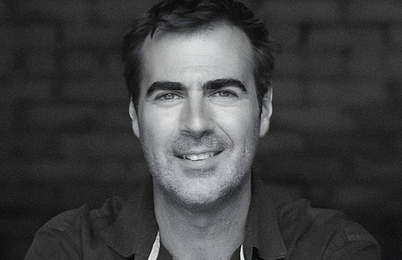Black and white close-up portrait of a man with short dark hair smiling at the camera.