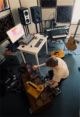 High-angle view of a person adjusting equipment in a music studio filled with speakers, keyboards, and guitars.