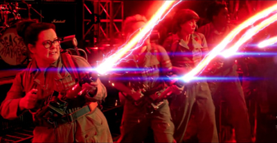 Four people in jumpsuits firing bright, glowing energy beams in a dark, red-lit setting.