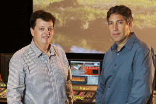 Two men standing in front of a large screen and a sound mixing console.