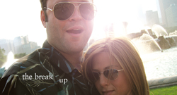 A man in sunglasses and a patterned shirt poses closely with a woman in sunglasses near a fountain.