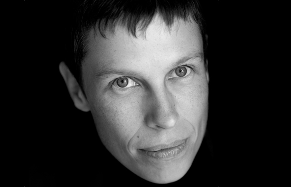 Black and white close-up portrait of a person looking directly at the camera against a dark background.