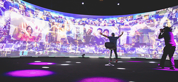 A person stands in front of a large, curved wall of digital screens showing various video feeds.