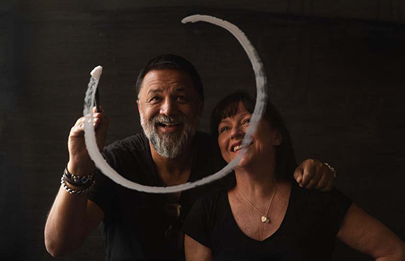 A smiling man and woman pose behind a glass pane with a white circle drawn around them.