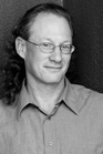 A man with glasses and long hair pulled back, wearing a button-down shirt.