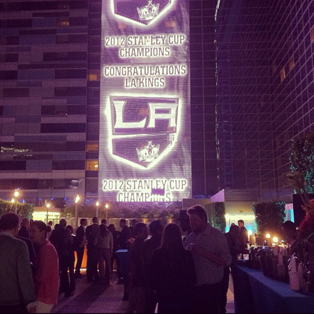 A large screen on a building displays "2012 Stanley Cup Champions Congratulations LA Kings" and the LA Kings logo. A crowd ga