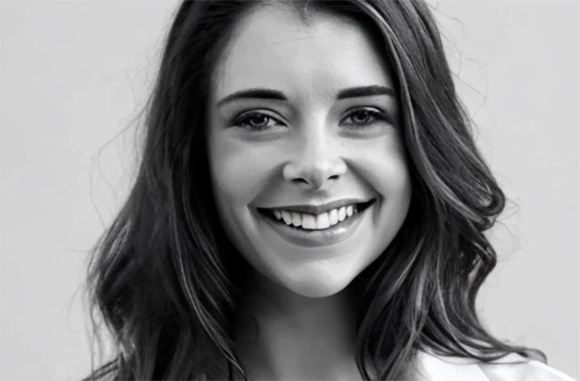 A smiling young woman with long wavy hair looking directly at the camera in a black and white portrait.