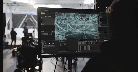 A person viewed from behind works on a computer monitor displaying a complex 3D wireframe model.