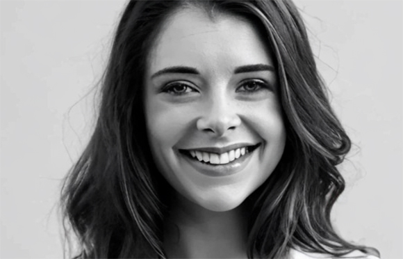 A smiling young woman with long wavy hair looking directly at the camera in a black and white portrait.