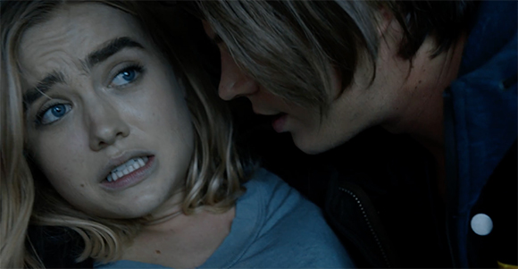 A distressed woman with blonde hair looks up at a man leaning toward her in a dark setting.